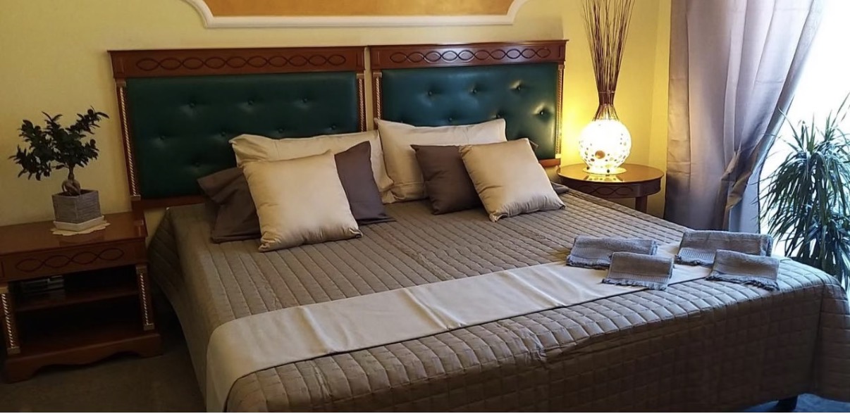 Camera matrimoniale con letto king size, testiera imbottita verde e comodini in legno